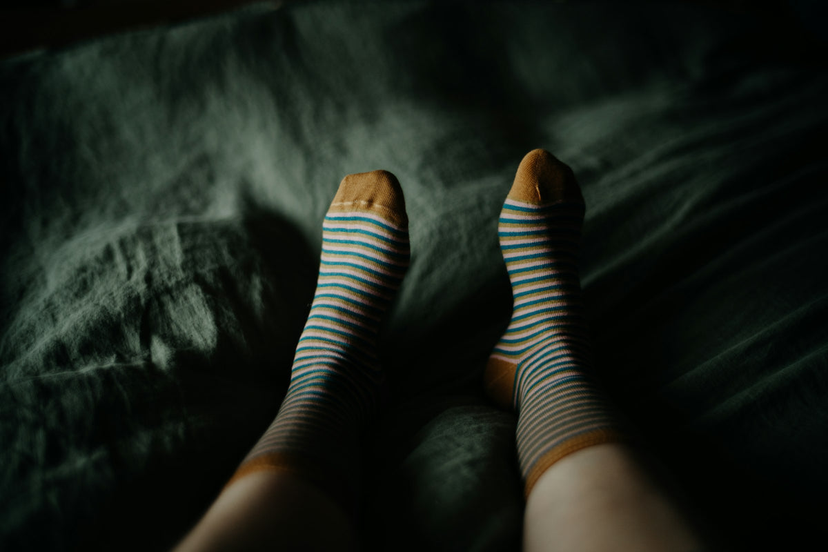 Woman's feet in blue and mustard striped socks resting on green bedding